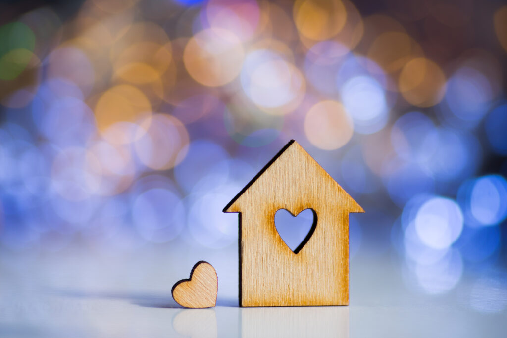 Das Bild zeigt ein aus Holz geschnitztes Haus mit einem Herz in der Mitte.