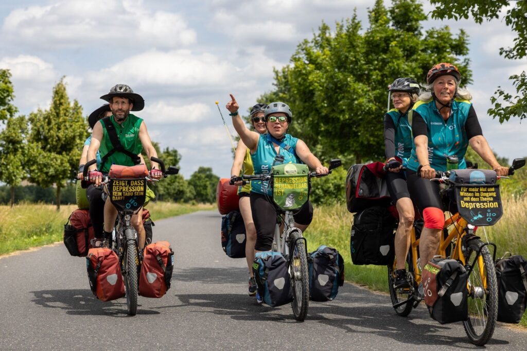Beitragsbild zur Mut-Tour 2026. Zu sehen sind mehrere Menschen auf Tandem-Rädern während der Mut-Tour.